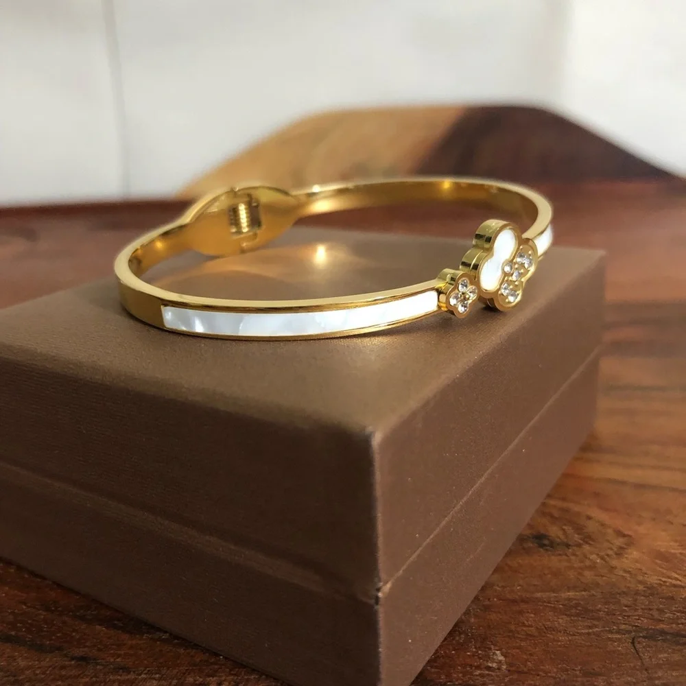 gold-toned hinged bangle bracelet featuring white clover motifs and crystal New
